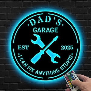 Puede incluir: Letrero de garaje de metal negro con un resplandor azul neón. El letrero dice "DAD'S GARAGE" con llave inglesa y destornillador cruzados, "EST 2025" y "I CAN FIX ANYTHING STUPID."