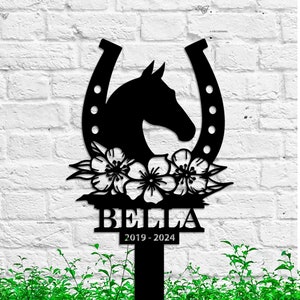 May include: Black metal silhouette of a horse's head inside a horseshoe with flowers and the name Bella and dates 2019-2024.