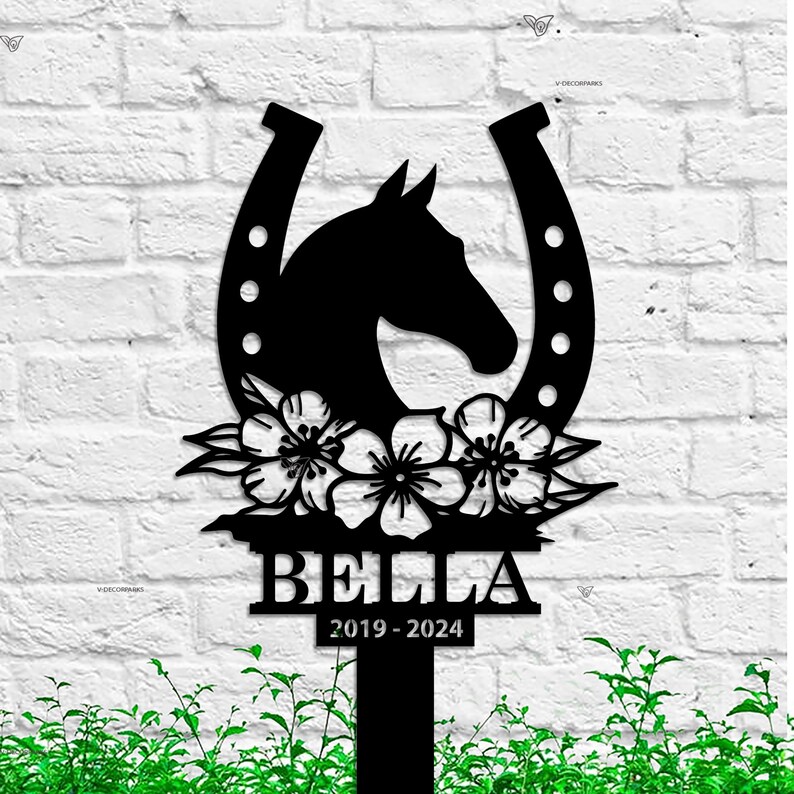 May include: Black metal silhouette of a horse's head inside a horseshoe with flowers and the name Bella and dates 2019-2024.