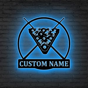 Può includere: Un'insegna al neon nera e blu con un tema da biliardo. L'insegna include un triangolo di palle da biliardo, stecche incrociate e la scritta "CUSTOM NAME" in una cornice rettangolare, il tutto all'interno di un design circolare. L'insegna è montata su un muro di mattoni.