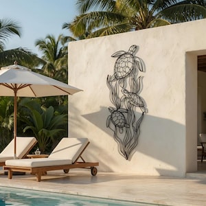 Op de afbeelding: Zwart metalen wandkunstwerk met drie zeeschildpadden die zwemmen tussen gestileerd zeewier. De schildpadden hebben gedetailleerde schildpatronen. Het kunstwerk is gemonteerd op een getextureerde witte muur, in een tropische buitenomgeving.