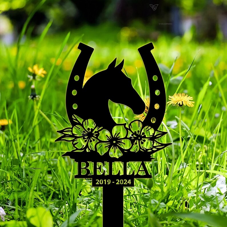 May include: Black metal garden stake featuring a horseshoe design, a horse head silhouette, and floral accents. The stake is engraved with the name "BELLA" and the dates "2019-2024".