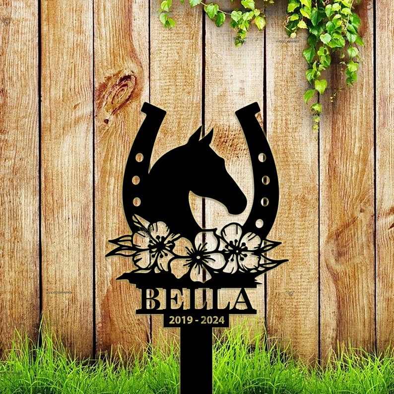 May include: Black metal garden stake featuring a horseshoe design, a horse head silhouette, and floral accents. The stake is engraved with the name "BELLA" and the dates "2019-2024".