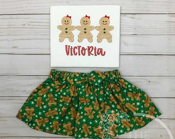 May include: A green skirt with a gingerbread pattern and a white shirt with three gingerbread people and the name "Victoria" embroidered on it.
