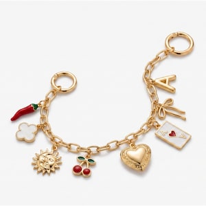 May include: A gold-tone chain bracelet featuring various charms including a red chili pepper, a white clover, a sun and moon face, red cherries, a heart, a playing card with a red heart, a bow, and the letter A.