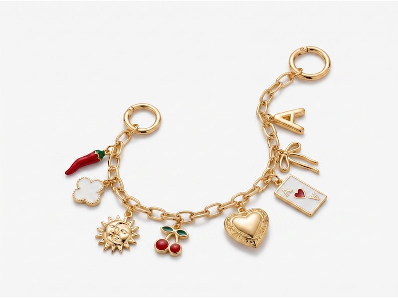 May include: A gold-tone chain bracelet featuring various charms including a red chili pepper, a white clover, a sun and moon face, red cherries, a heart, a playing card with a red heart, a bow, and the letter A.