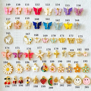 May include: A collection of colorful charms in various shapes, including butterflies, flowers, and fruit. The charms are in shades of pink, purple, blue, yellow, and gold. Each charm has a small loop for attaching to jewelry or other crafts.