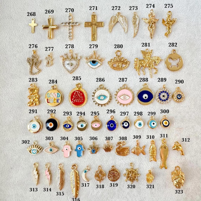 May include: A collection of gold-colored charms, including crosses, angel wings, and various pendants with intricate designs. Some charms feature text like "Good Luck" and "Be Free". The charms are suitable for jewelry making.