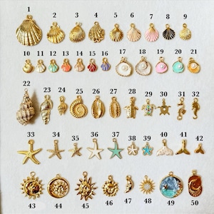 May include: A collection of fifty gold-toned metal charms in various shapes including seashells, starfish, seahorses, and suns, numbered one through fifty. Some charms feature enamel accents in pink, blue, white, and red, while others include small pearls.