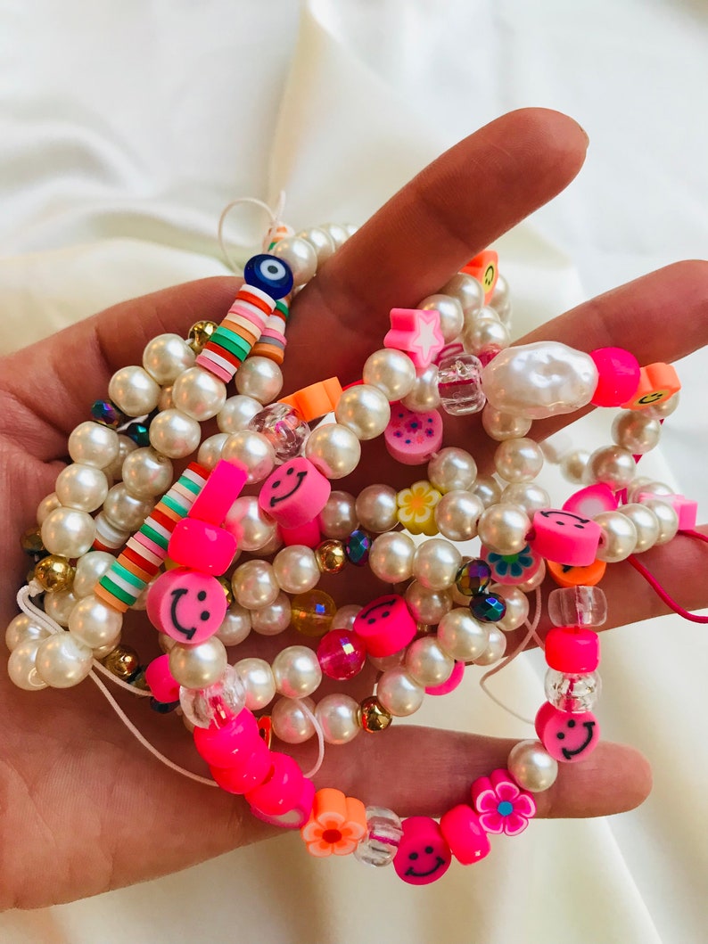 May include: Several beaded bracelets with white faux pearls, neon pink smiley faces, and colourful accent beads. Some bracelets include flower and star-shaped beads, and an evil eye charm.