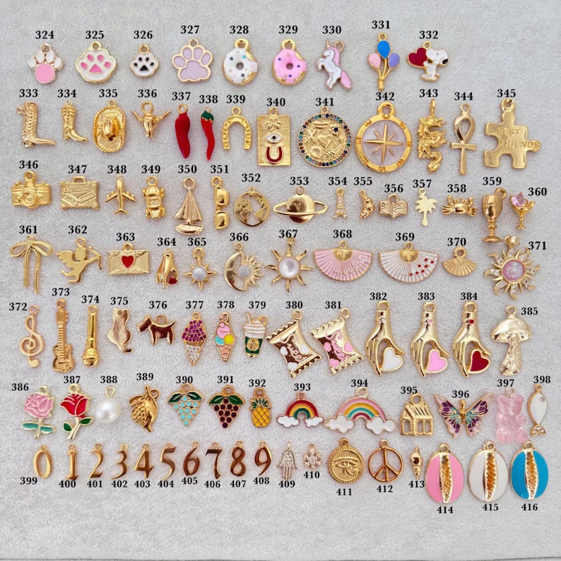 May include: A collection of gold-toned charms with various designs, including animals, food, symbols, and numbers. Some charms feature enamel details in colors like pink, red, and blue. The charms are suitable for jewelry making.