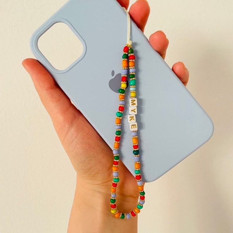 May include: A beaded phone charm with the name "MYKE" spelled out in white letter beads. The charm features a colorful pattern of red, green, orange, yellow, and purple beads, attached to a light blue phone case.