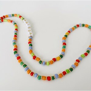 May include: A colorful beaded lanyard with the name "ANISSA" spelled out in white letter beads. The lanyard features a variety of beads in red, orange, yellow, green, and blue, with gold-colored spacers. A white string is attached.