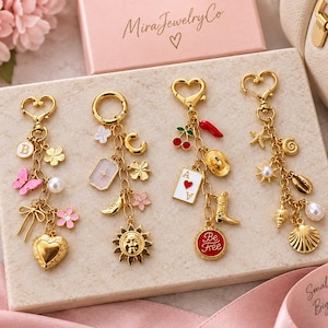 May include: Four gold-toned metal keychains featuring various charms including a heart, butterfly, letter B, sun, moon, playing card with a heart, cowboy boot, chili pepper, cherry, and seashells, with one charm reading Be Free.