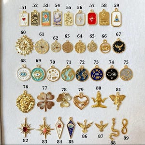 May include: A collection of metal charms numbered 51 through 89, featuring various shapes including rectangles, circles, hearts, stars, and figures. The charms display enamel details, symbols like eyes, celestial bodies, and animals in gold tones.