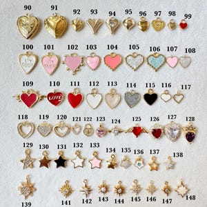 May include: A collection of metal charms in heart and star shapes, numbered 90 through 148. The charms feature various finishes including gold, enamel, glitter, and clear stones. Some hearts display text like I'M GOOD or LOVE.