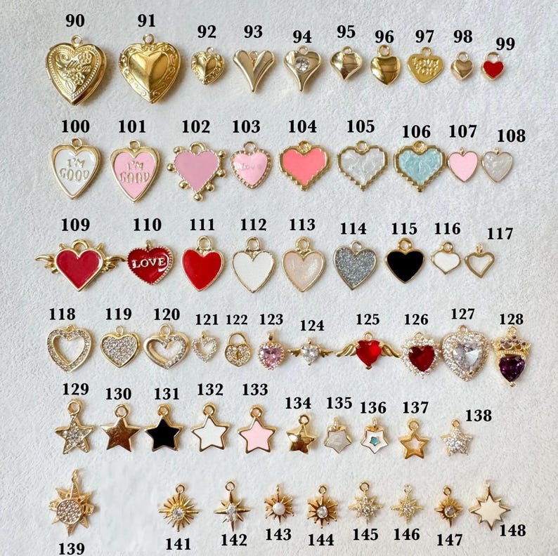 May include: A collection of metal charms in heart and star shapes, numbered 90 through 148. The charms feature various finishes including gold, enamel, glitter, and clear stones. Some hearts display text like I'M GOOD or LOVE.