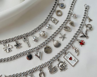 May include: Three silver-toned metal chain charm bracelets featuring an assortment of dangling charms including a key, a pearl shell, a four-leaf clover, a smiley face, a sun, a swan, a horseshoe, a ladybug, a peace sign, and an ace of hearts playing card.