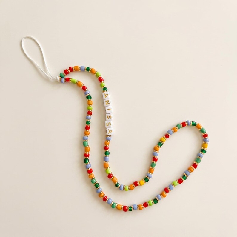 May include: A colorful beaded lanyard with the name "ANISSA" spelled out in white letter beads. The lanyard features a variety of small, round beads in red, orange, yellow, green, blue, and gold. A white cord is attached at the top.