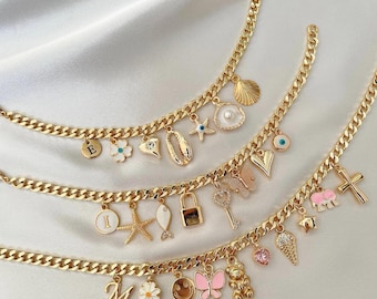 May include: Three gold chain bracelets with various charms, including a seashell, a heart, a cross, a lock, a fish, a starfish, a daisy, a smiley face, a butterfly, a teddy bear, an ice cream cone, a pink heart, an elephant, a key, and a pearl. The charms are in white, pink, and blue.
