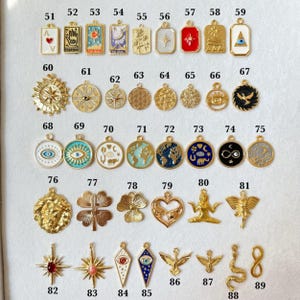 May include: A collection of gold-toned metal charms arranged in rows and numbered 51 through 89. The charms feature various designs including celestial symbols, eyes, animals, flowers, and geometric shapes, some with colorful enamel accents.