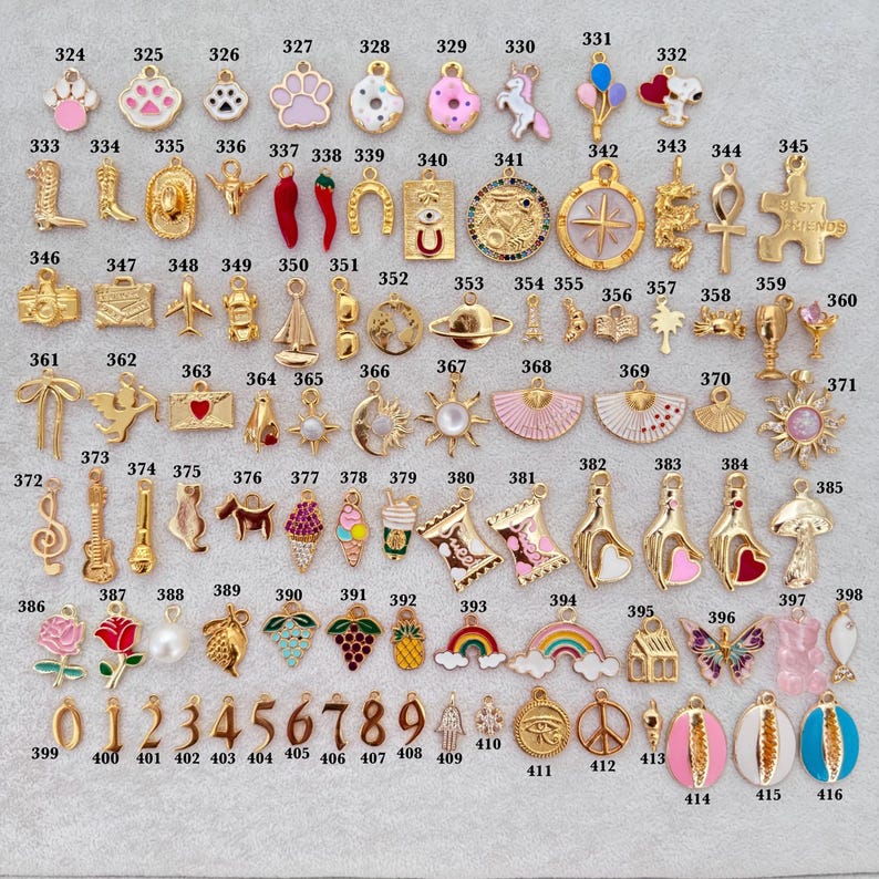 K&ouml;nnte beinhalten: Eine Sammlung goldfarbener Charms mit verschiedenen Designs, darunter ein Pfotenabdruck, ein Cowboy-Stiefel, ein Hufeisen, ein Regenbogen und ein Schmetterling. Die Charms sind nummeriert und eignen sich f&uuml;r die Schmuckherstellung oder zum Basteln. Draufsicht.