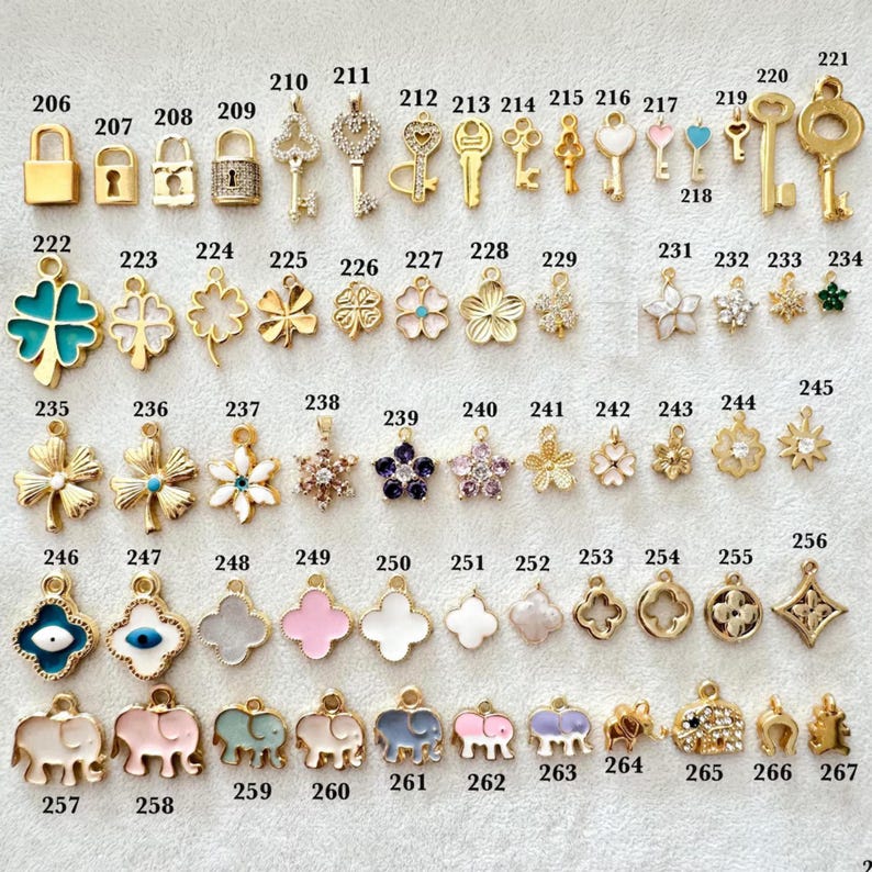 May include: A collection of gold-toned charms and pendants, including keys, locks, clovers, flowers, and animal shapes. Some charms feature colorful enamel details, and others are adorned with crystals. The charms are numbered for easy selection.