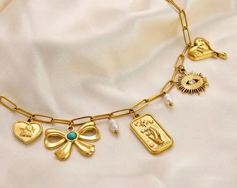 May include: Gold-toned necklace with multiple charms, including a heart with an angel, a bow with a turquoise center, a rectangular pendant with a hand, a sun with an eye, and a heart-shaped charm. The necklace also features small pearl accents.