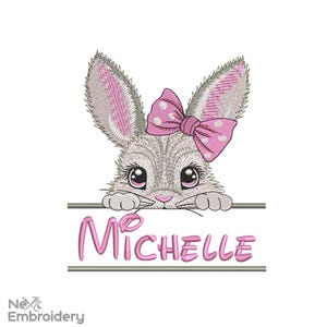 Könnte beinhalten: Stickerei eines grauen Kaninchens mit rosa Ohren und einer rosa Schleife mit weißen Punkten, die über einem Banner mit dem Namen "Michelle" in rosa Schrift schaut.