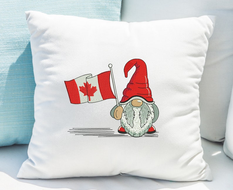 May include: White pillow with embroidered image of a gnome holding a Canadian flag. The gnome is wearing a red hat and has a white beard.