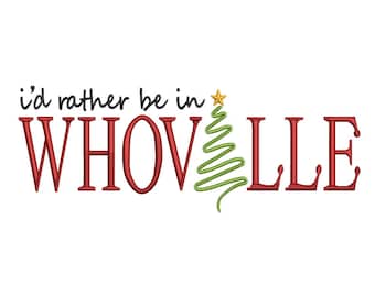 May include: An embroidery design featuring the black text 'i'd rather be in' above the red text 'WHOVLLE'. The letter 'O' in 'WHOVLLE' is replaced by a green, stylized, zigzag-patterned Christmas tree topped with a small yellow star.