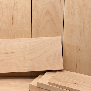 May include: A collection of light-colored, smooth-surfaced wooden boards arranged in a stack. The planks feature a natural, pale tan grain pattern with subtle variations in tone and texture, showcasing the raw, unfinished appearance of the wood.