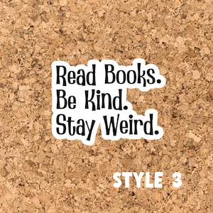 May include: A corkboard with a white sticker that says "Read Books. Be Kind. Stay Weird." in black text. The sticker is on a brown corkboard with the words "STYLE 3" in white text below the sticker.