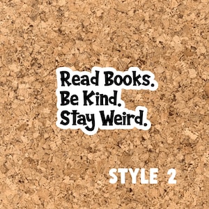May include: A corkboard with a black and white sticker that reads "Read Books. Be Kind. Stay Weird." The sticker is on a corkboard background. The text "STYLE 2" is printed in white below the sticker.