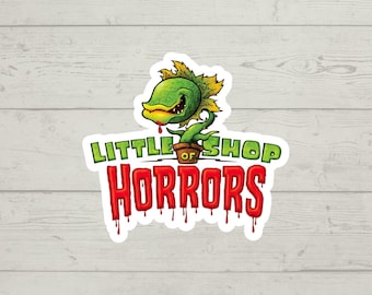 Puede incluir: Una pegatina con una ilustración de dibujos animados de una planta verde con una sonrisa de dientes y sangre roja goteando. El texto "Little Shop of Horrors" está escrito en rojo con sangre goteando.