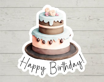 Può includere: Una torta a due piani con glassa marrone e blu chiaro, decorata con fiori rosa e bianchi e codette di cioccolato. La torta è su un piatto marrone e il testo "Happy Birthday!" è scritto in corsivo nero.