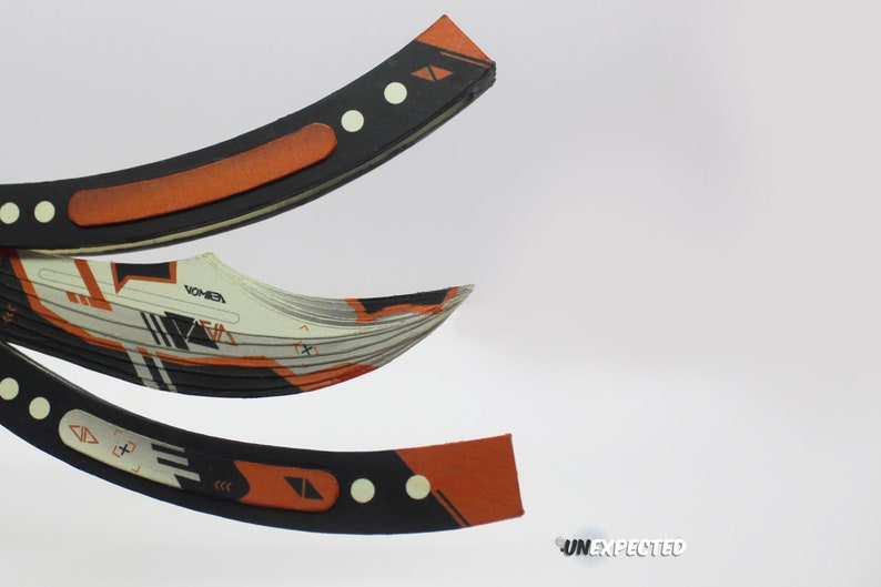 May include: A black and orange folding knife with a geometric pattern and the word "VOMER" printed on the blade.