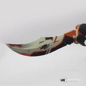 May include: A black and orange butterfly knife with a white and orange patterned blade. The blade is open and the knife is in a throwing position.