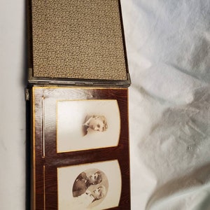 May include: A vintage photo album with a brown leather cover and gold accents. The album is open to reveal two black and white photos of people.