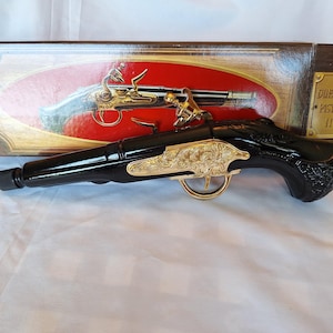 May include: A black decorative pistol with gold accents, featuring ornate detailing. The pistol is displayed with its original box, which has an image of the pistol and the text "DUELING PISTOL 11".