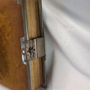 May include: A vintage photo album with a brown velvet cover and a silver metal clasp. The album is closed and the clasp is fastened.