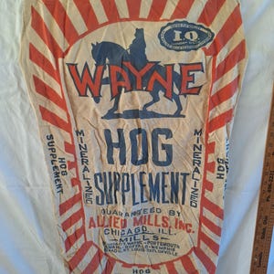 May include: Vintage Wayne Hog Supplement feed sack. The beige sack features red and white stripes, with the words "WAYNE HOG SUPPLEMENT" in blue and red. The sack is marked "100 LBS. NET" and includes the Allied Mills, Inc. logo.