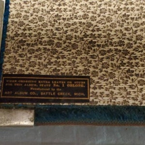 May include: A vintage photo album with a floral pattern cover. The album is made by Art Album Co. in Battle Creek, Michigan. The text on the cover reads: "When ordering extra leaves or stubs for this album, state No. 1 oblong."