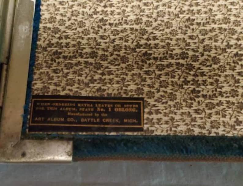 May include: A vintage photo album with a floral pattern cover. The album is made by Art Album Co. in Battle Creek, Michigan. The text on the cover reads: "When ordering extra leaves or stubs for this album, state No. 1 oblong."