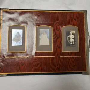 May include: A vintage photo album with a dark brown wood-grain cover and three photo slots. Each slot has a gold trim and contains a black and white photo of a baby.