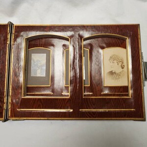 May include: A vintage wooden photo album with two open pages. Each page has a gold-trimmed frame with a black mat and a black and white photograph inside.