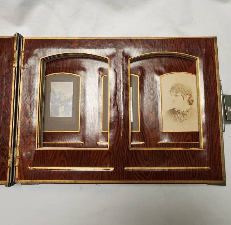 May include: A vintage wooden photo album with two open pages. Each page has a gold-trimmed frame with a black mat and a black and white photograph inside.