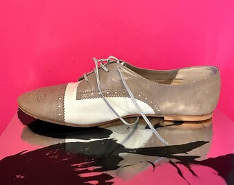 May include: A pair of grey and white leather shoes with laces. The shoes have a brogue design and a rounded toe.