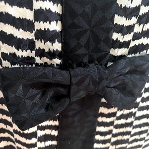 May include: A black and white striped dress with a black bow at the waist.