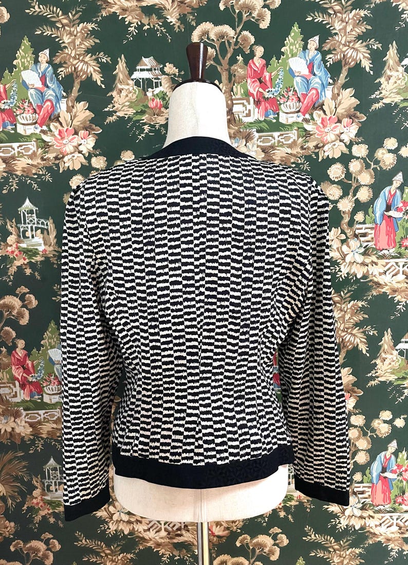 May include: A black and white striped long-sleeved cardigan with a black trim around the neckline and hem.